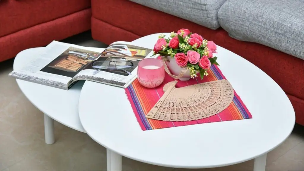 This white nested table is an unusual shape.  The large magazine is open across the two tables.  This is a perfect example of the use of these nested tables.
